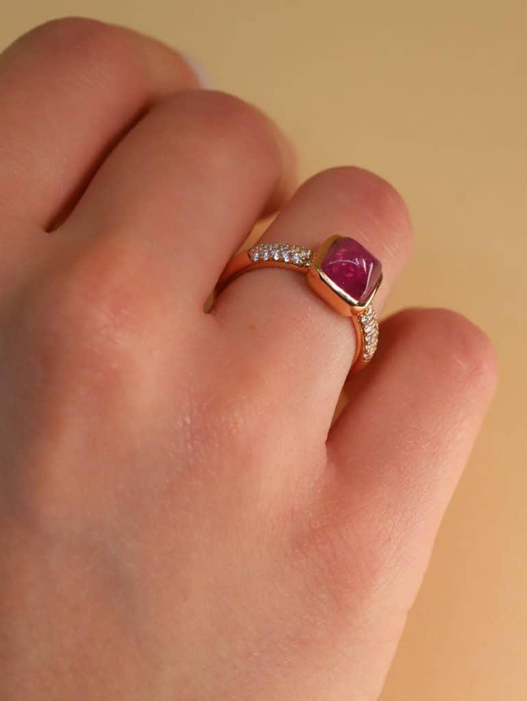 Bague en or avec pierre précieuse rouge et diamants sur doigt.