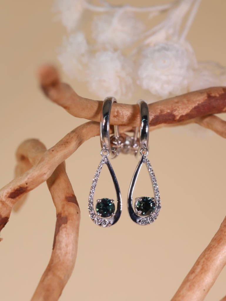 Boucles d'oreilles avec pierres vertes et cristaux sur branche en bois.